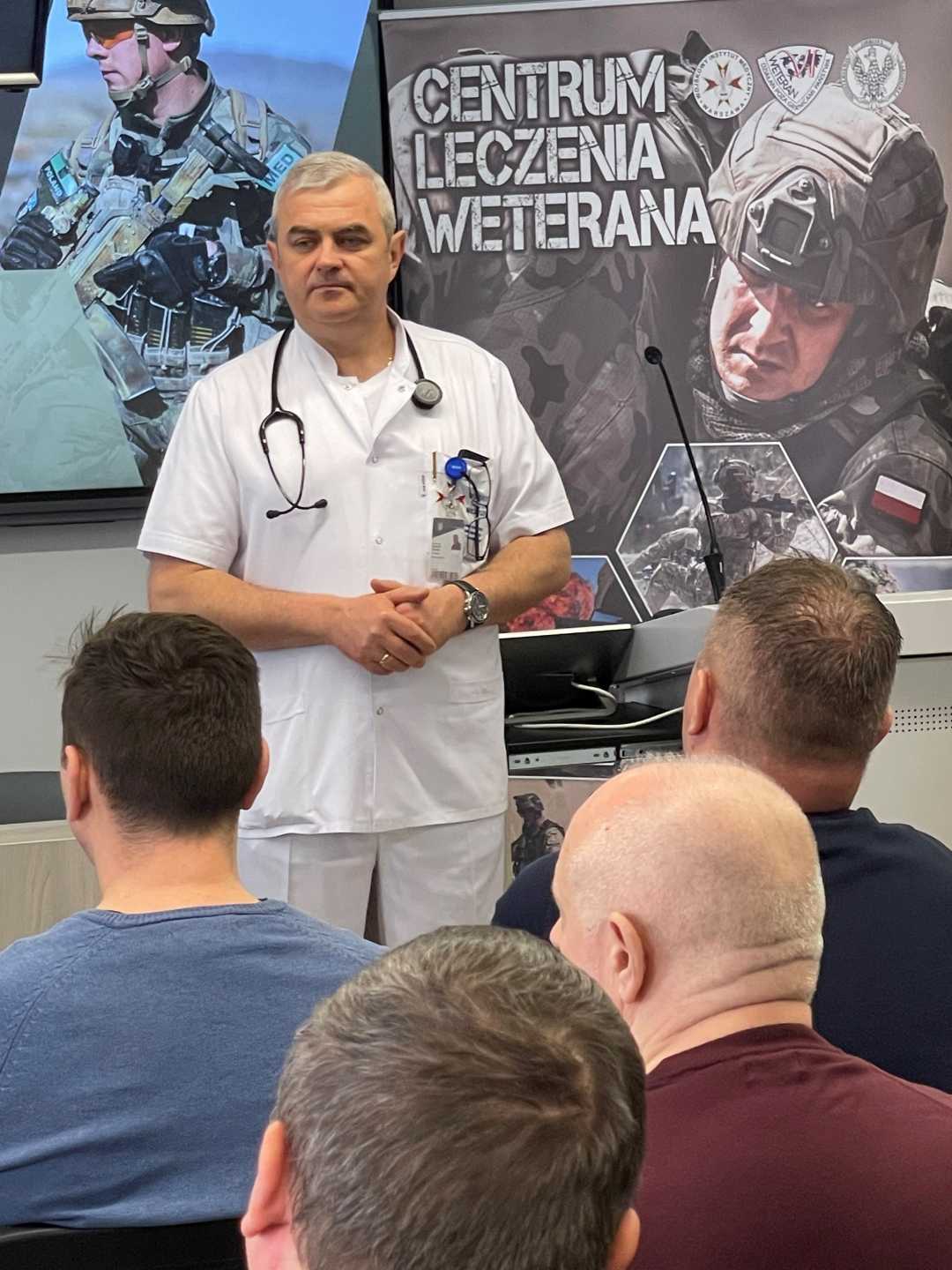 Jarosław Swistak przy mównicy podczas wykładu, za nim ekran z wyświetlaną prezentacją.