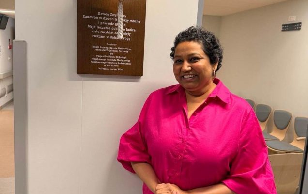 Uśmiechnięta pacjentka stoi przy dzwonie zwycięzcy.