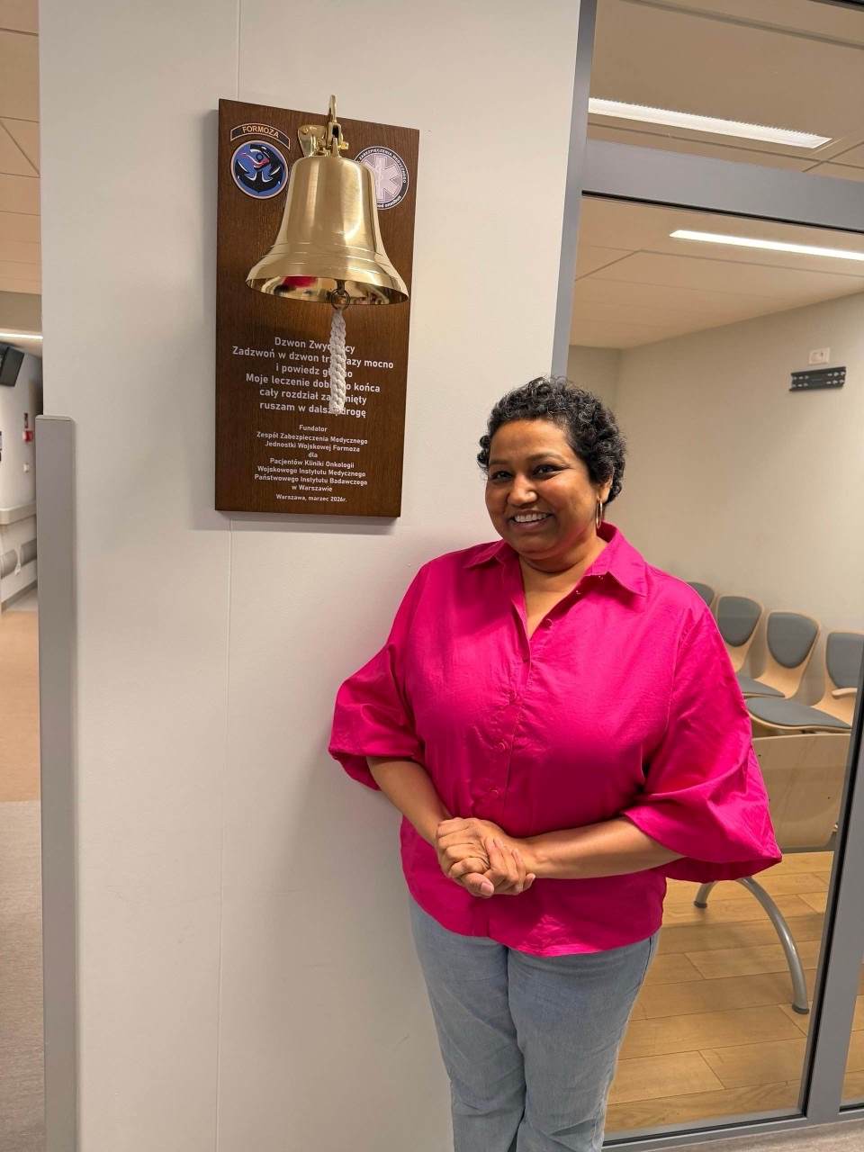 Uśmiechnięta pacjentka stoi przy dzwonie zwycięzcy.