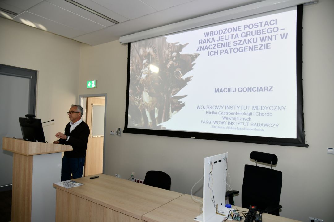 Maciej Gonciarz przy mównicy na sali WIM. Za nim wyświetlony slajd z prezentacji.
