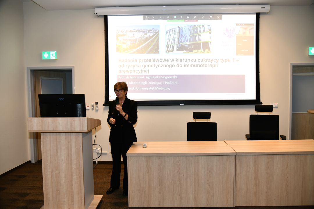 Agnieszka Szypowska z mikrofonem w ręku, podczas wykładu w sali LOMTI. Za nią tablica z prezentacją.