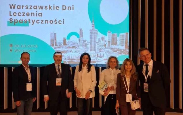 Prelegenci pozują do zdjęcia z a nimi na wyświetlaczu plansza wydarzenia.