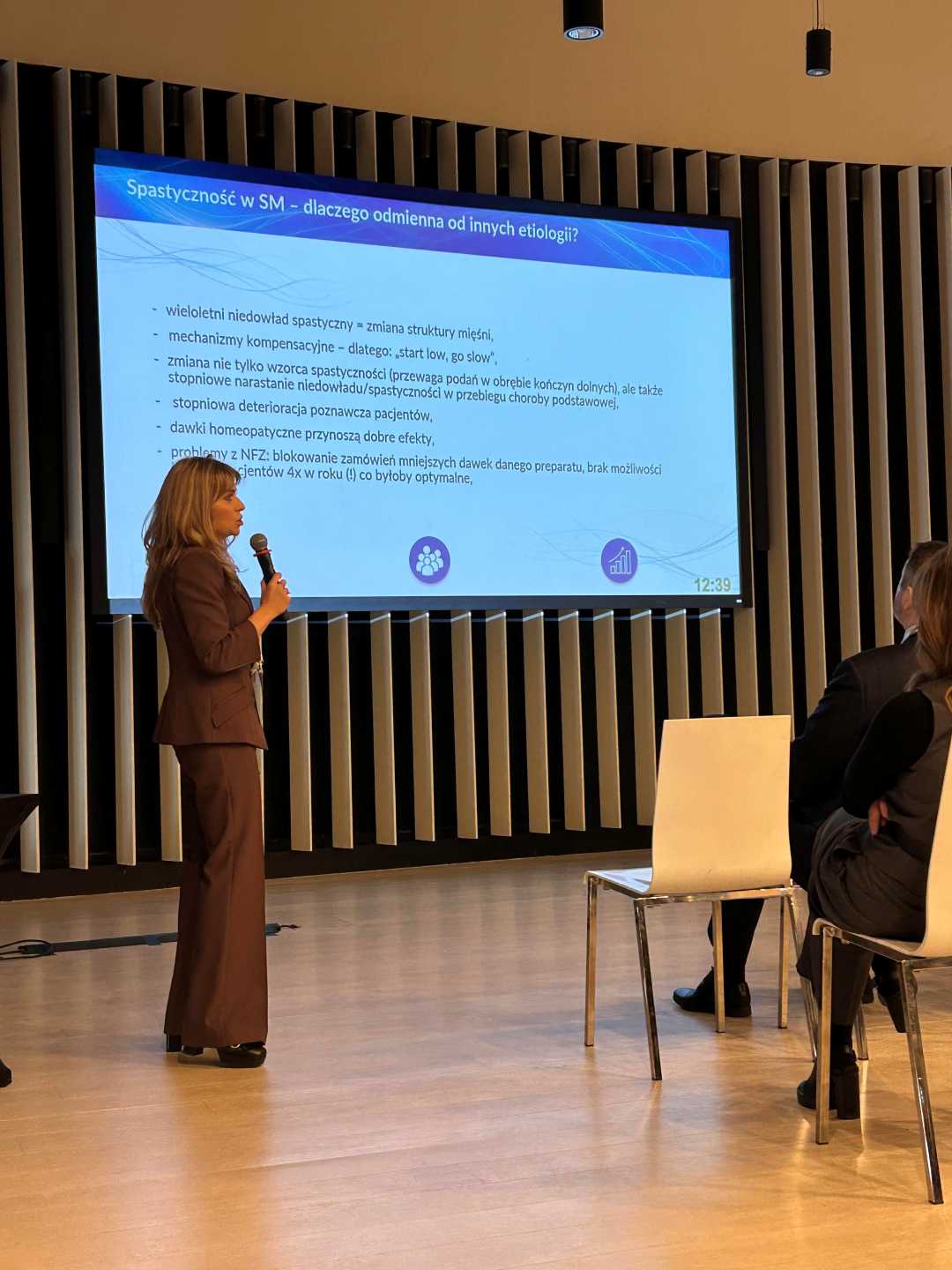 Katarzyna Gniadek-Olejniczak prowadzi prelekcję. Za nią wyświetlacz ze slajdem prezentacji.