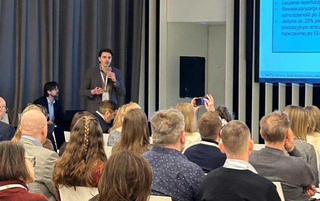 Ujęcie z tyłu sali słuchaczy i prelegenta podczas wykładu na sali konferencyjnej.