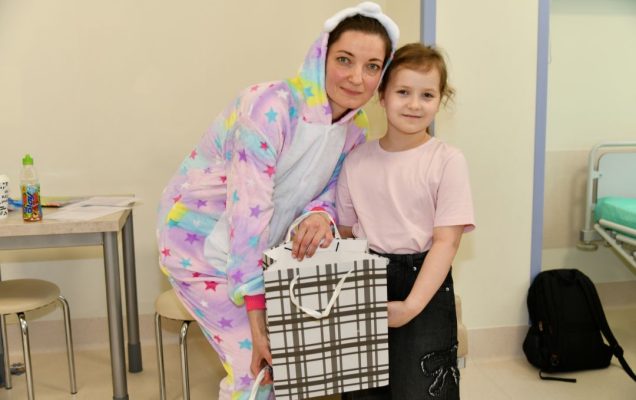 Sala szpitalna, dziewczynka odbiera prezent od pani w stroju wielkanocnym.