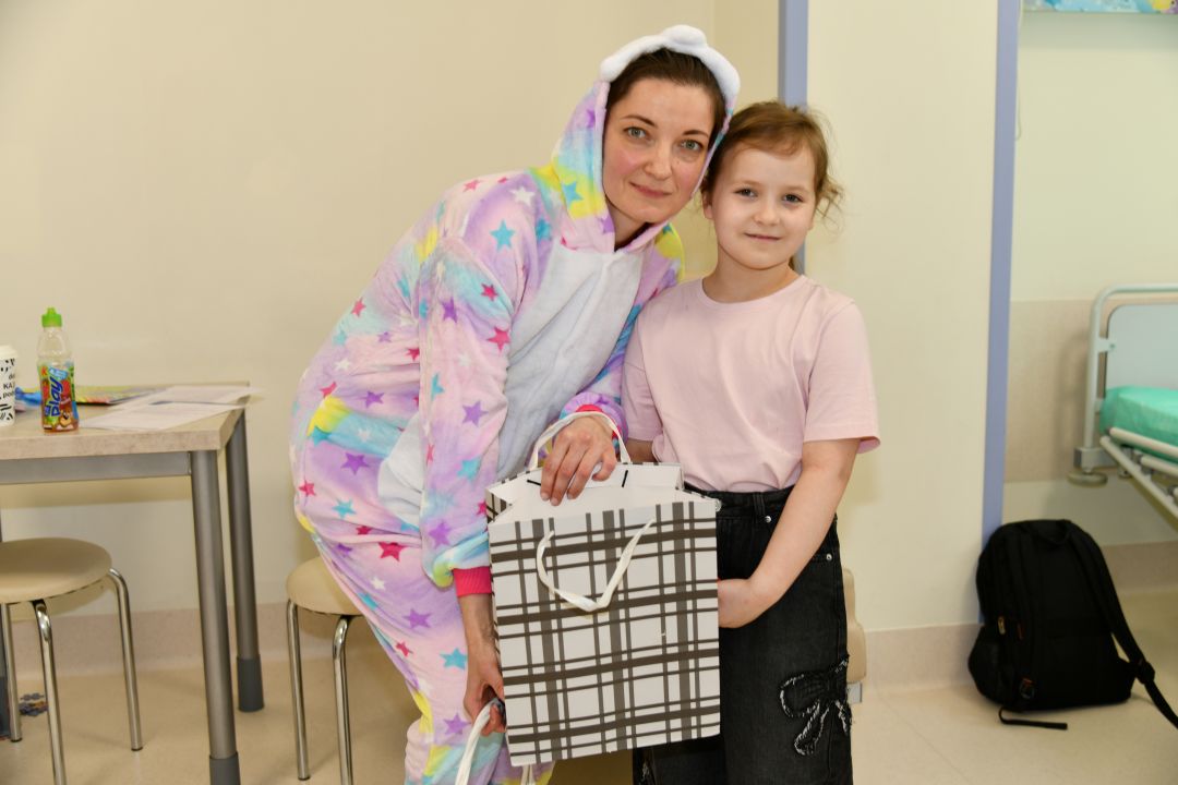 Sala szpitalna, dziewczynka odbiera prezent od pani w stroju wielkanocnym.