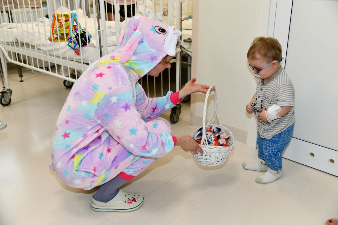 Zajączek wielkanocny z koszyczkiem ze słodyczami kuca przy małym pacjencie.