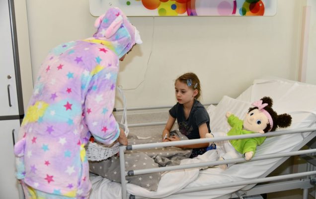 Zajączek wielkanocny w sali szpitalnej wręcza prezent dziewczynce siedzącej na łóżku.