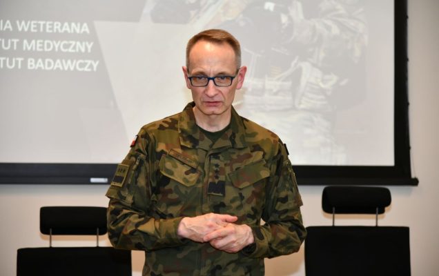 Grzegorz Gielerak za nim na wielkim ekranie wyświetlony slajd z prezentacji.