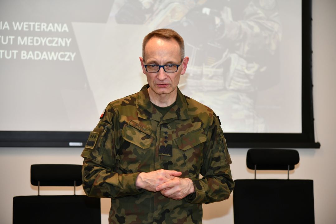 Grzegorz Gielerak za nim na wielkim ekranie wyświetlony slajd z prezentacji.