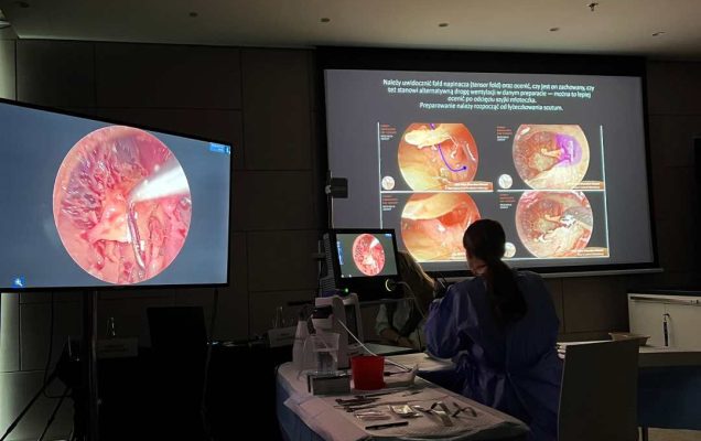 Przyciemniona sala. Przy stole laboratoryjnym siedzi mężczyzna. Przed nim na dwóch ekranach widok preparatów mikroskopowych.