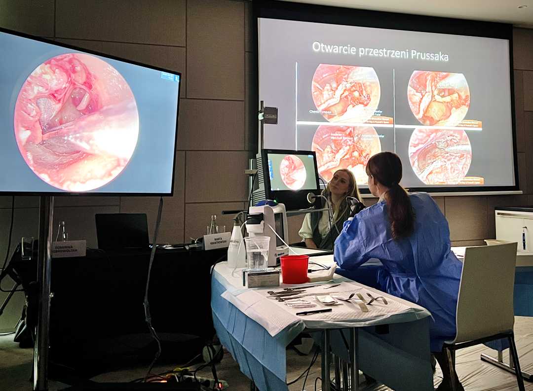 Przyciemniona sala. Przy stole laboratoryjnym siedzą dwie młode kobiety. Przed nimi na dwóch ekranach widok preparatów mikroskopowych.