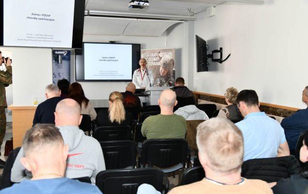 Ujęcie z tyłu sali na słuchaczy wykładu i prowadzącego wykład Piotra Dąbrowieckiego.