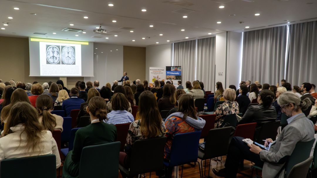Siedzący słuchacze podczas konferencji. Na wprost nich ekran z wyświetlaną prezentacją.