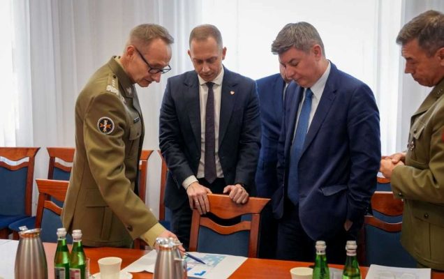 Cezary Tomczyk, Jan Grabiec, Roman Smogorzewsk, Grzegorz Gielerak stoją przy stole i omawiają leżący na nim dokument.