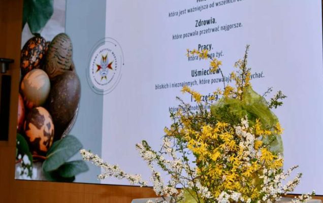 Stroik wielkanocny na auli WIM za nim wyświetlone na ekranie życzenia wielkanocne.