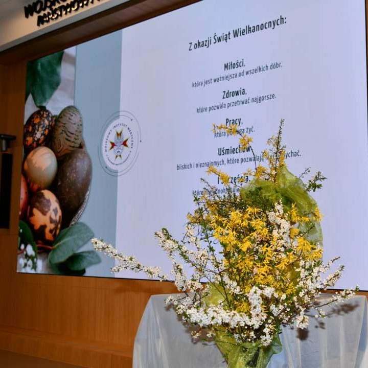 Stroik wielkanocny na auli WIM za nim wyświetlone na ekranie życzenia wielkanocne.