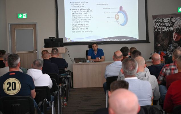 Siedzący słuchacze podczas wykładu. Za plecami prelegenta na wyświetlaczu plansza prezentacji.