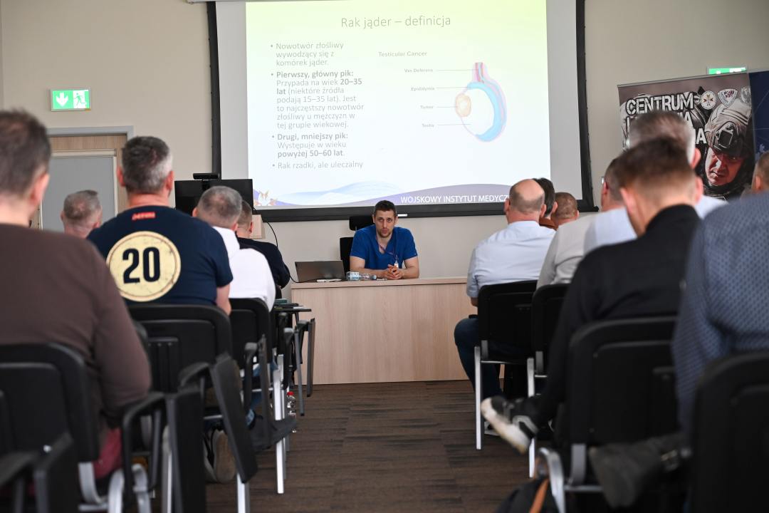 Siedzący słuchacze podczas wykładu. Za plecami prelegenta na wyświetlaczu plansza prezentacji.