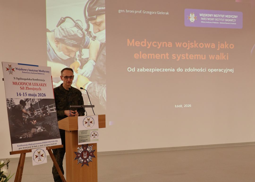 Dyrektor WIM przy mównicy, za jego plecami na ekranie slajd z konferencji.