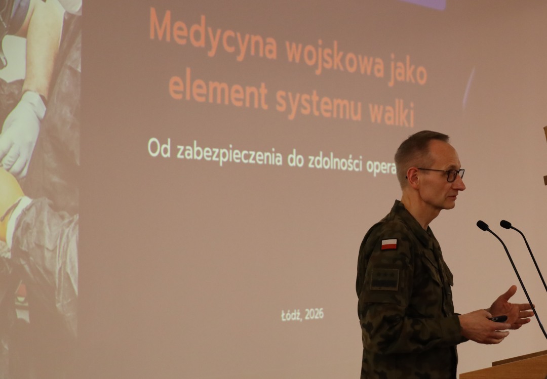 Dyrektor WIM przy mównicy, za jego plecami na ekranie slajd z konferencji.