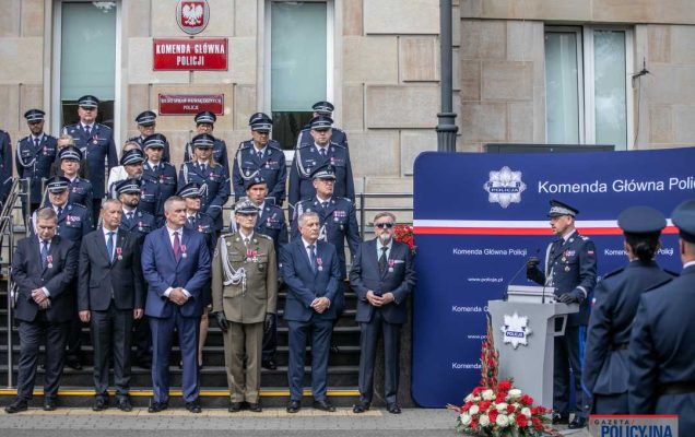 Zdjęcie grupowe przed budynkiem policji oznaczonych laureatów medalu oraz pracownikami policji.