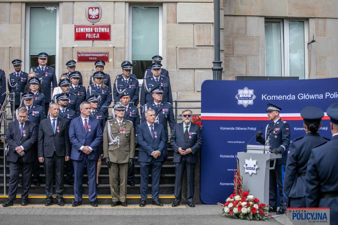 Zdjęcie grupowe przed budynkiem policji oznaczonych laureatów medalu oraz pracownikami policji.