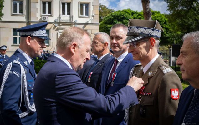 Czesław Mroczek przypina Dyrektorowi WIM medal przed gmachem policji.