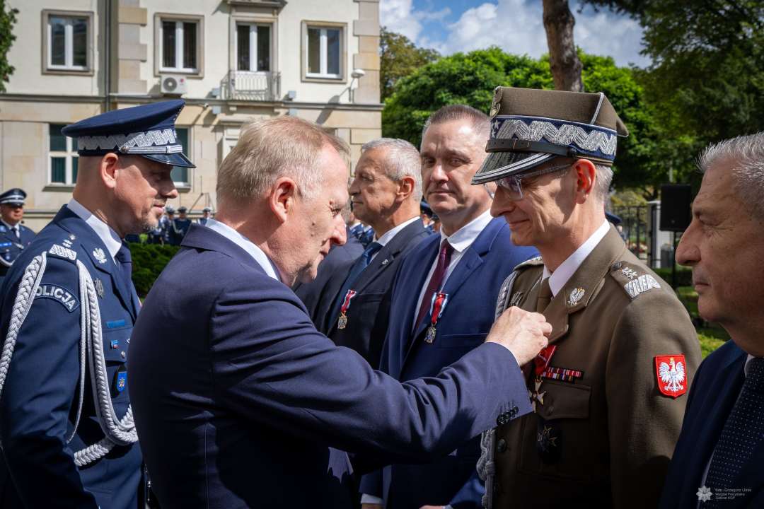 Czesław Mroczek przypina Dyrektorowi WIM medal przed gmachem policji.
