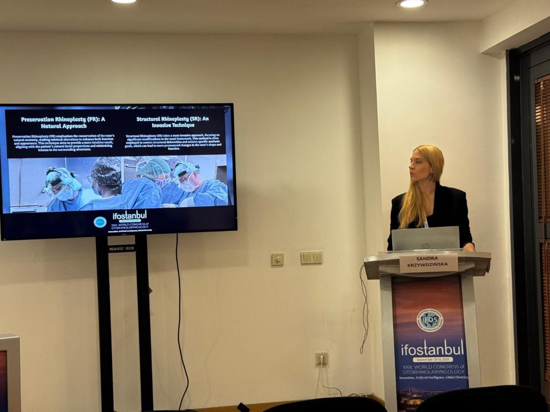 Prelegentka przy mównicy podczas prelekcji. Obok niej na ekranie wyświetlony slajd z konferencji.