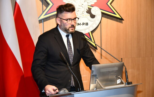Piotr Chojan przy mównicy, za nim dwie flagi Polski oraz logo WIM