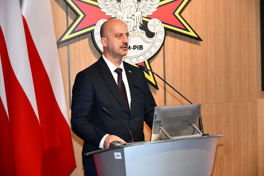 Mirosław Bryś przy mównicy. Za jego plecami flaga Polski i logotyp WIM-PIB.