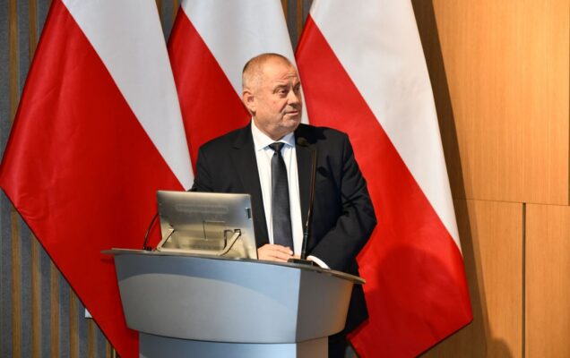 Alojzy Nowak przy mównicy. Za jego plecami flaga Polski i logotyp WIM-PIB.